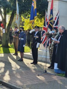 A Remembrance Day ceremony at a memorial with forces personnel holding flags.