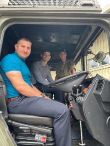 3 men in the cab of a large army vehicle