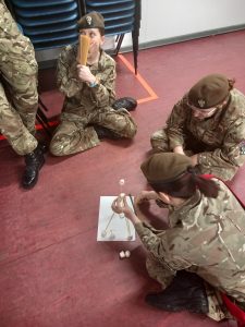 3 female Army Cadets sitting on the floor joining spaghetti strands with marshmallows.