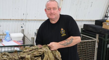 Fletch stands beside a large crate filled with Cadet kits inside a warehouse.